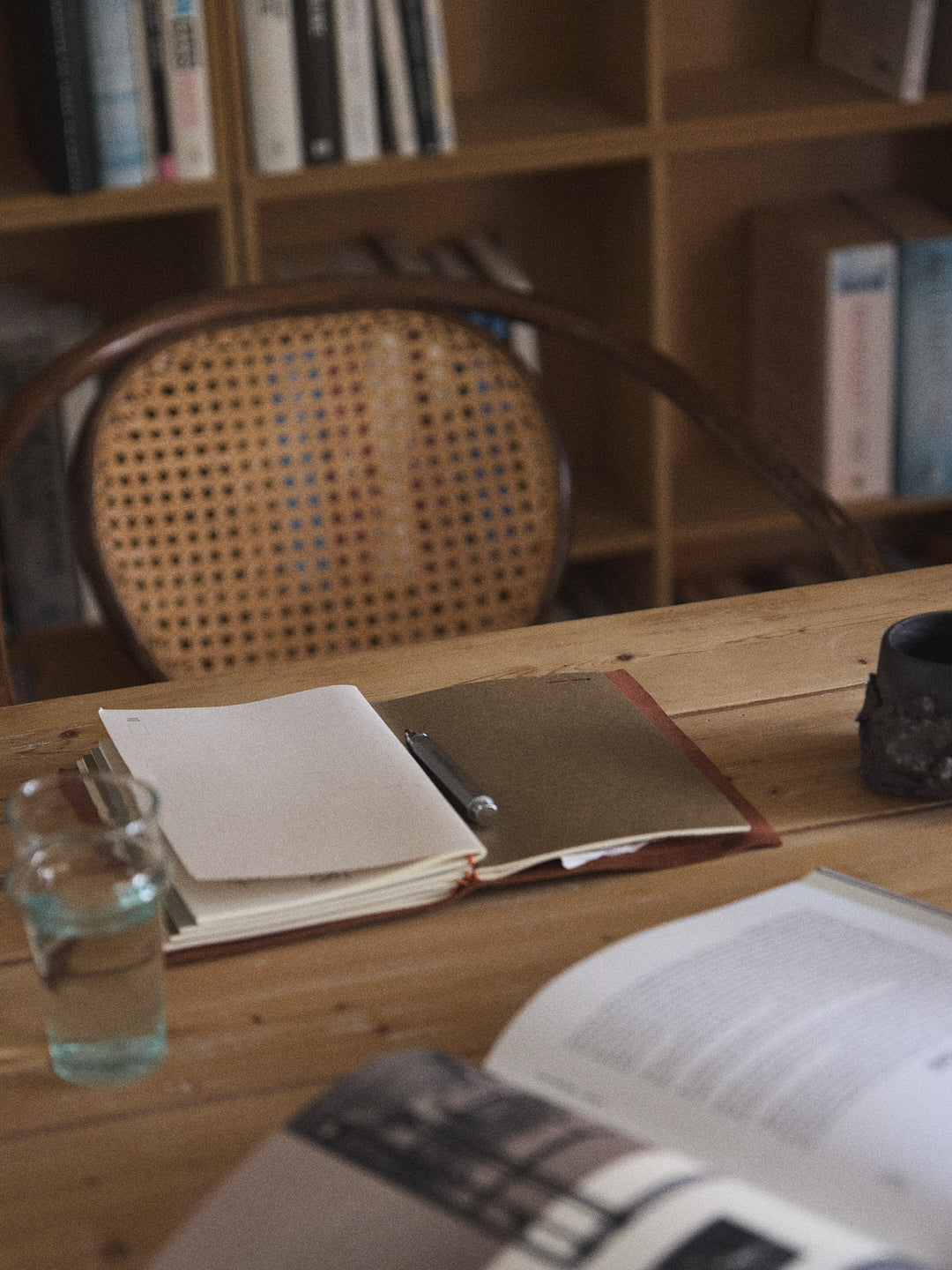 Wooden table with books, a glass of water, and a notebook in a cozy room.