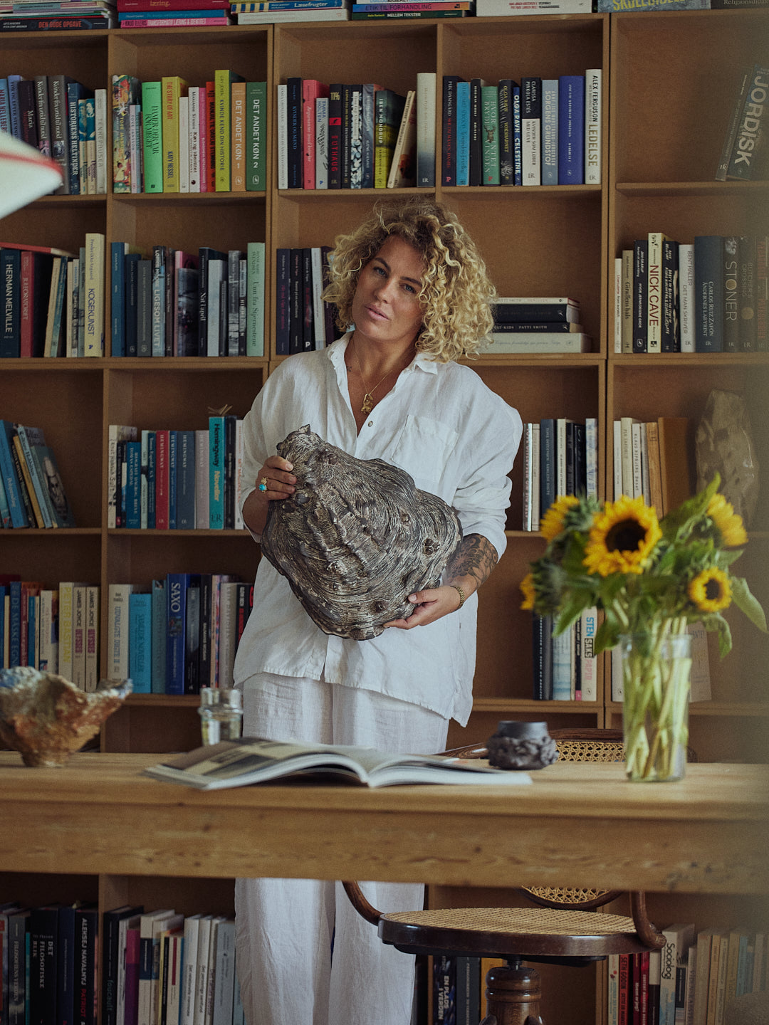 Woman holding a ceramic art piece in front of a bookshelf filled with books.